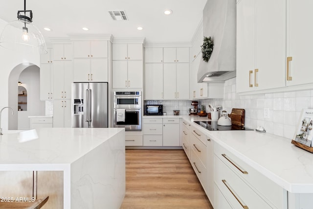 kitchen with black appliances, tasteful backsplash, white cabinets, decorative light fixtures, and wall chimney exhaust hood