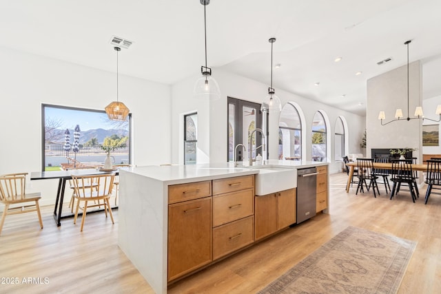 kitchen featuring sink, light hardwood / wood-style flooring, hanging light fixtures, and a center island with sink