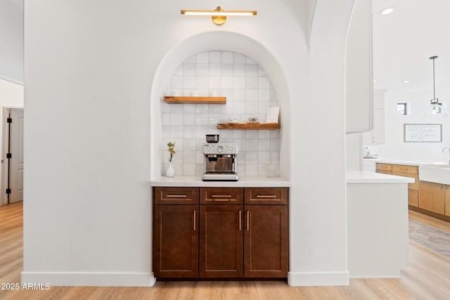 bar with hanging light fixtures, sink, light hardwood / wood-style floors, decorative backsplash, and dark brown cabinetry