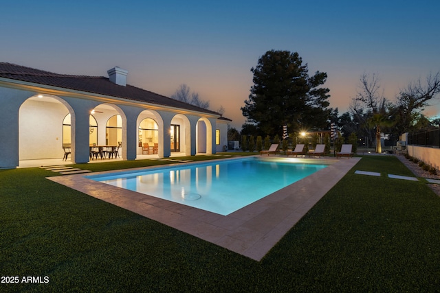 pool at dusk with a patio and a lawn