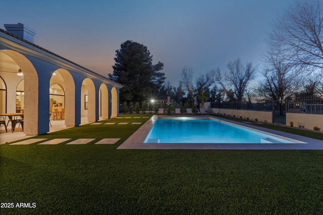 pool at dusk with a patio area and a yard