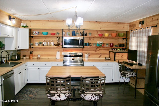 kitchen with appliances with stainless steel finishes, white cabinetry, dark wood-type flooring, wooden walls, and sink