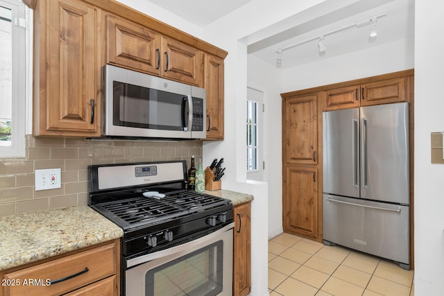 kitchen with light stone counters, backsplash, stainless steel appliances, and light tile patterned flooring