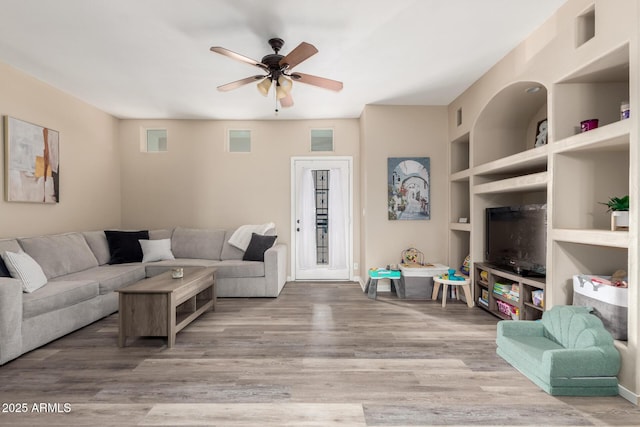 living room featuring hardwood / wood-style flooring, built in features, and ceiling fan