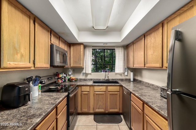 kitchen with sink, dark stone countertops, light tile patterned floors, appliances with stainless steel finishes, and a raised ceiling