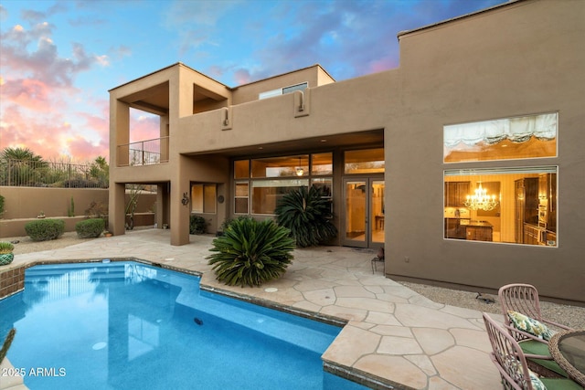 back house at dusk featuring a balcony, a fenced in pool, and a patio