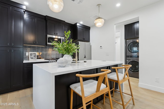 kitchen with a kitchen island with sink, hanging light fixtures, light hardwood / wood-style floors, and stacked washing maching and dryer