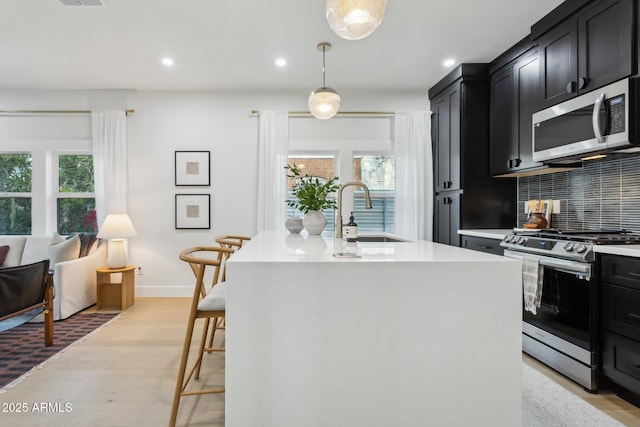 kitchen featuring sink, decorative light fixtures, a center island with sink, appliances with stainless steel finishes, and decorative backsplash