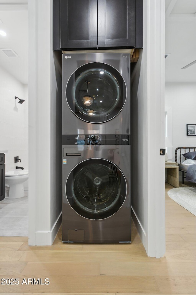 laundry room with stacked washer and clothes dryer and light wood-type flooring