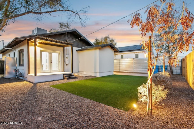 back house at dusk featuring a lawn and french doors