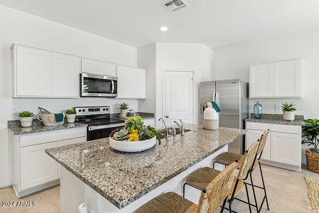 kitchen with sink, stainless steel appliances, a kitchen breakfast bar, white cabinets, and a center island with sink