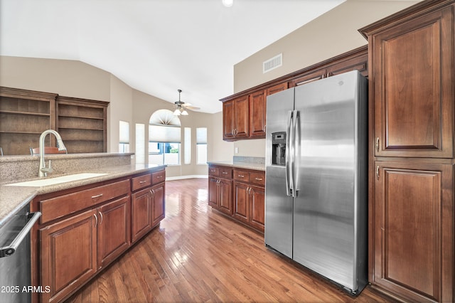 kitchen with vaulted ceiling, appliances with stainless steel finishes, sink, dark hardwood / wood-style flooring, and light stone counters