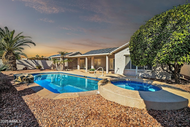 pool at dusk featuring a patio and an in ground hot tub