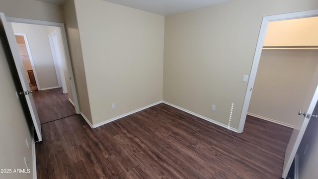 unfurnished bedroom featuring dark wood-style floors, a spacious closet, baseboards, and a closet