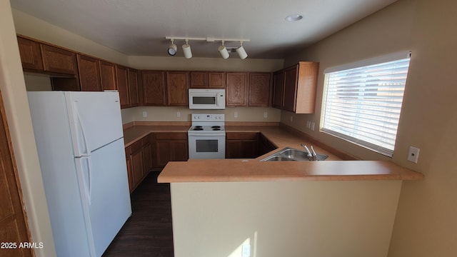 kitchen featuring a peninsula, white appliances, light countertops, and a sink