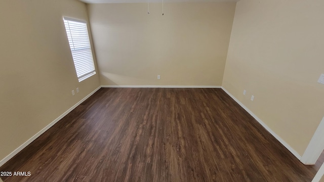 spare room featuring dark wood-type flooring and baseboards