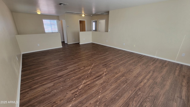 empty room with dark wood-type flooring, visible vents, and baseboards