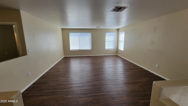 unfurnished room with dark wood-type flooring, visible vents, and baseboards