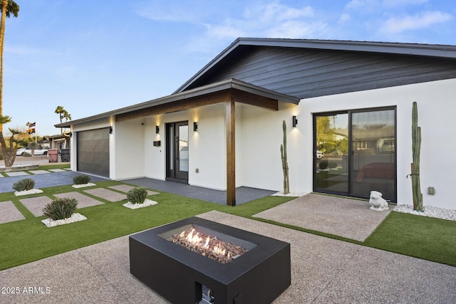 rear view of house with a patio, stucco siding, a lawn, an outdoor fire pit, and a garage