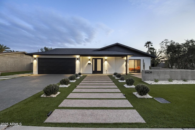 mid-century modern home featuring stucco siding, an attached garage, a front yard, fence, and driveway