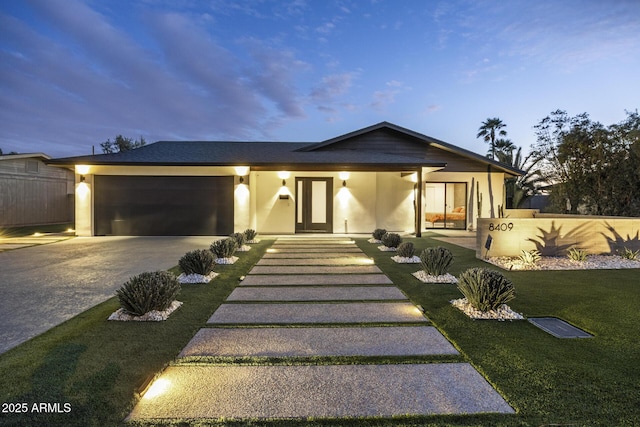 view of front facade featuring an attached garage, driveway, a lawn, and stucco siding