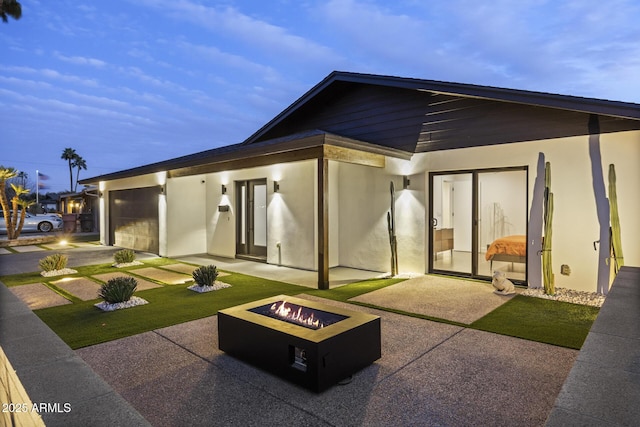 rear view of property with stucco siding, a lawn, an outdoor fire pit, a patio area, and a garage