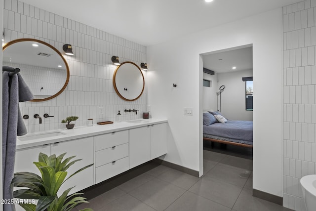 ensuite bathroom with double vanity, a sink, tile walls, and tile patterned floors