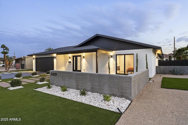 view of front facade featuring an attached garage, driveway, fence, and a front lawn