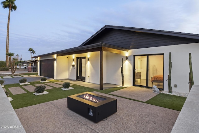 rear view of property featuring a yard, a patio, stucco siding, a garage, and a fire pit