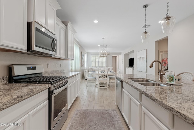 kitchen with stainless steel appliances, a sink, visible vents, hanging light fixtures, and light wood-type flooring