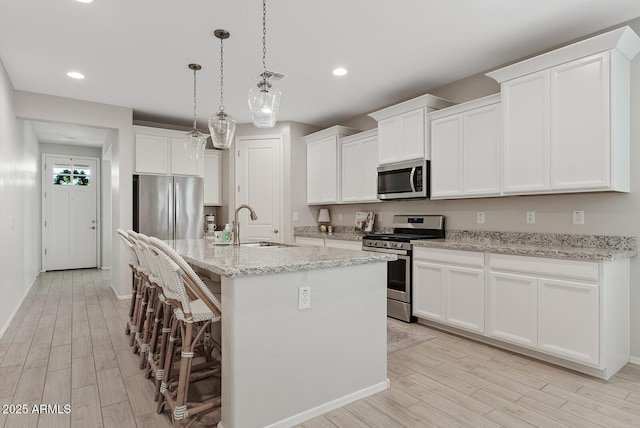 kitchen featuring a kitchen island with sink, a sink, appliances with stainless steel finishes, light wood finished floors, and a kitchen bar