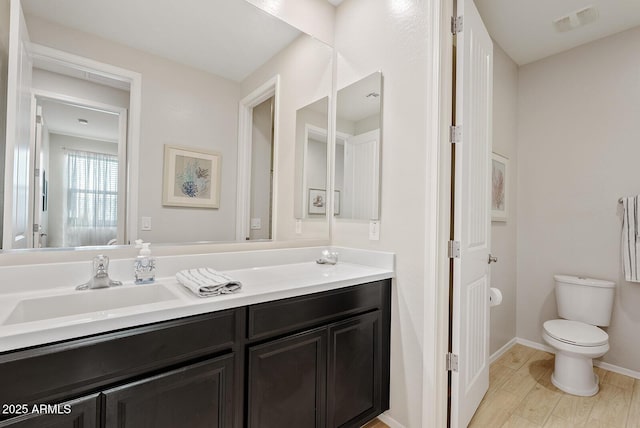 bathroom with toilet, wood finished floors, vanity, visible vents, and baseboards