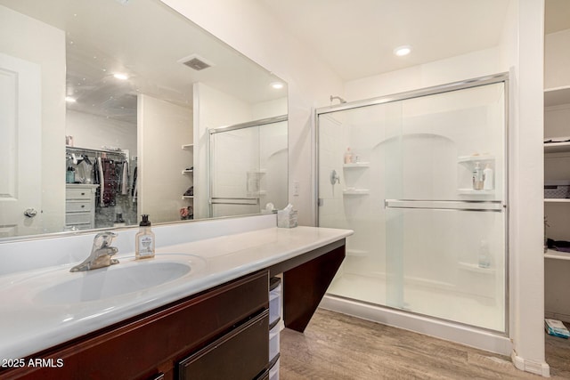 bathroom featuring wood finished floors, vanity, a walk in closet, visible vents, and a stall shower