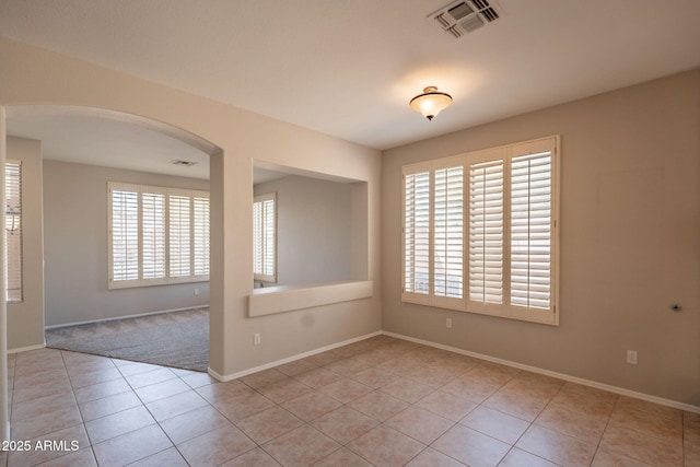 empty room with arched walkways, baseboards, visible vents, and light tile patterned flooring