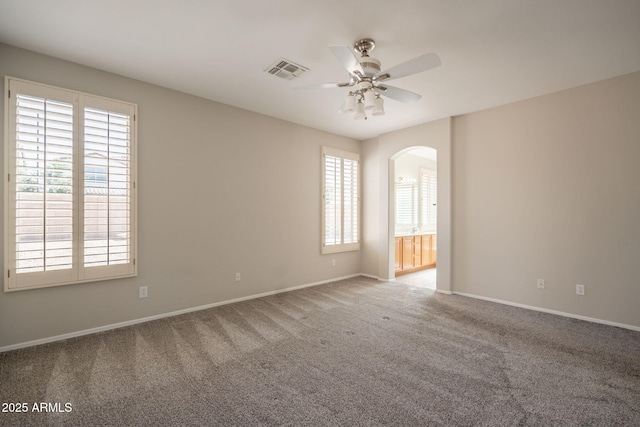 spare room with carpet floors, arched walkways, baseboards, and ceiling fan