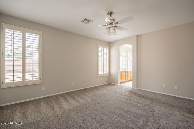spare room with carpet floors, arched walkways, baseboards, and ceiling fan