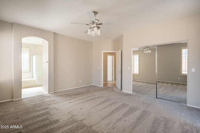unfurnished bedroom featuring arched walkways, baseboards, a closet, connected bathroom, and carpet flooring