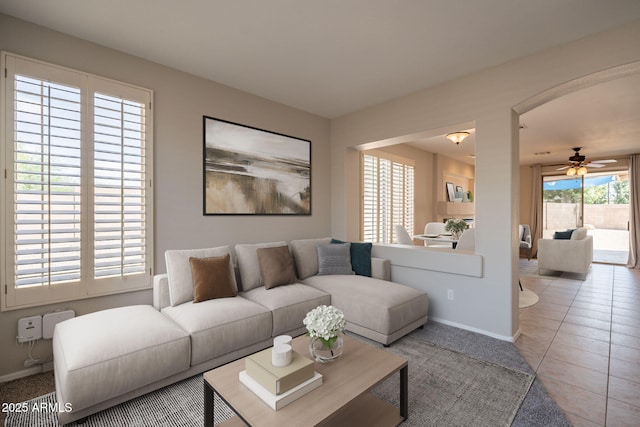 tiled living area featuring a ceiling fan, baseboards, and arched walkways