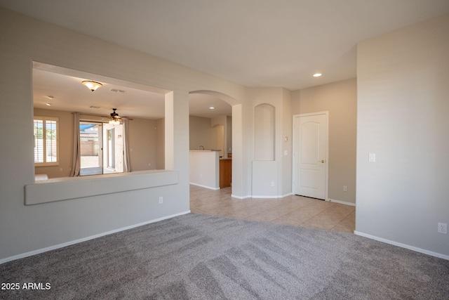 tiled empty room featuring carpet floors, arched walkways, baseboards, and ceiling fan
