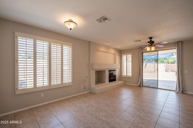 unfurnished living room with visible vents, a glass covered fireplace, baseboards, ceiling fan, and light tile patterned floors