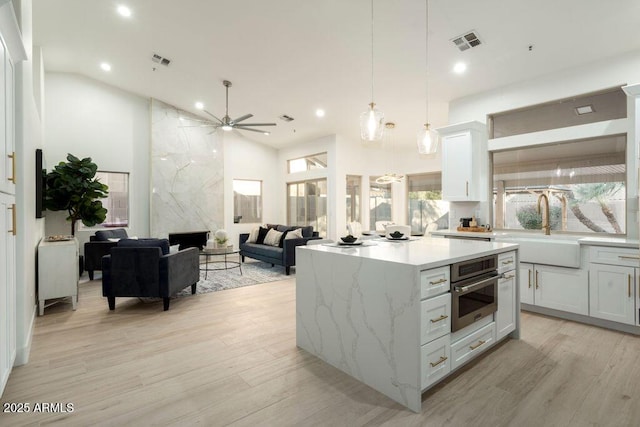 kitchen with decorative light fixtures, high vaulted ceiling, a kitchen island, oven, and white cabinets