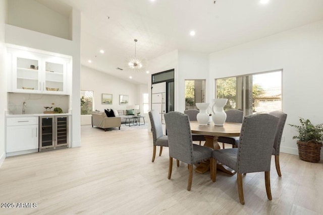 dining space featuring a high ceiling, a notable chandelier, wine cooler, and light hardwood / wood-style floors