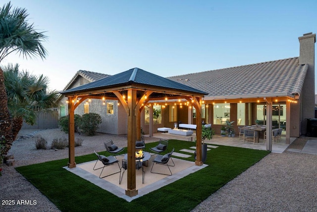 back house at dusk featuring a gazebo and a patio area