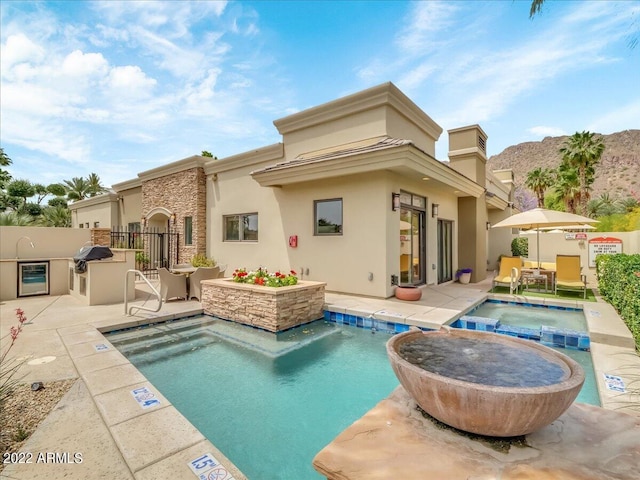 rear view of house featuring a patio, exterior kitchen, pool water feature, a pool with hot tub, and a mountain view