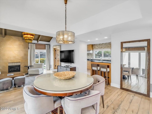 dining space featuring vaulted ceiling with beams, a notable chandelier, a fireplace, and light hardwood / wood-style floors