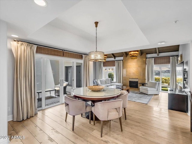 dining area featuring a tile fireplace, a tray ceiling, and light hardwood / wood-style flooring