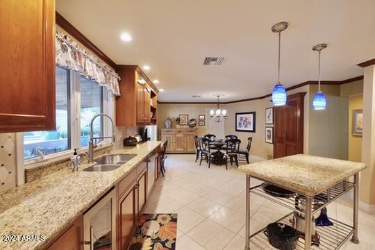 kitchen featuring hanging light fixtures, an inviting chandelier, light stone countertops, ornamental molding, and sink