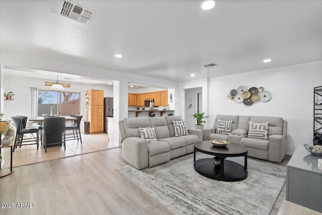 living room featuring light wood-style flooring, visible vents, and recessed lighting