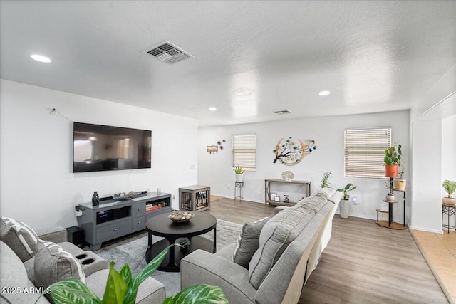 living room featuring light wood-style flooring, visible vents, a textured ceiling, and recessed lighting