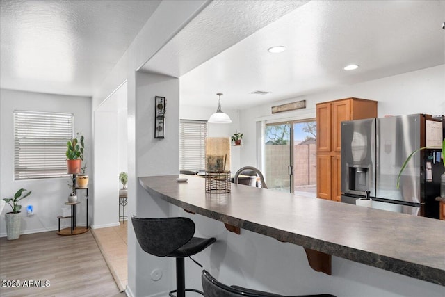 kitchen featuring dark countertops, a kitchen bar, brown cabinetry, and stainless steel fridge with ice dispenser